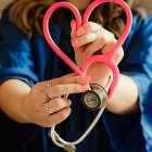  Pflegerin, die mit einem neonfarbenen Stethoskop ein Herz formt