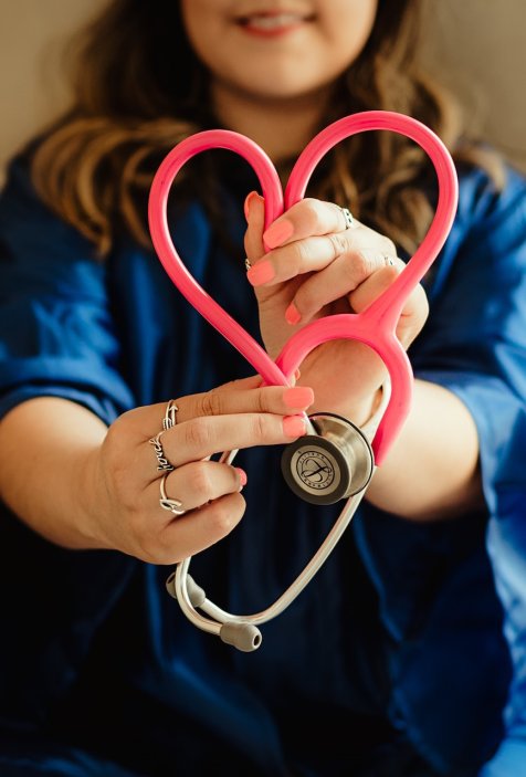  Pflegerin, die mit einem neonfarbenen Stethoskop ein Herz formt